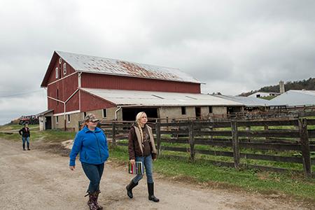 Two women walking past red barn on farm