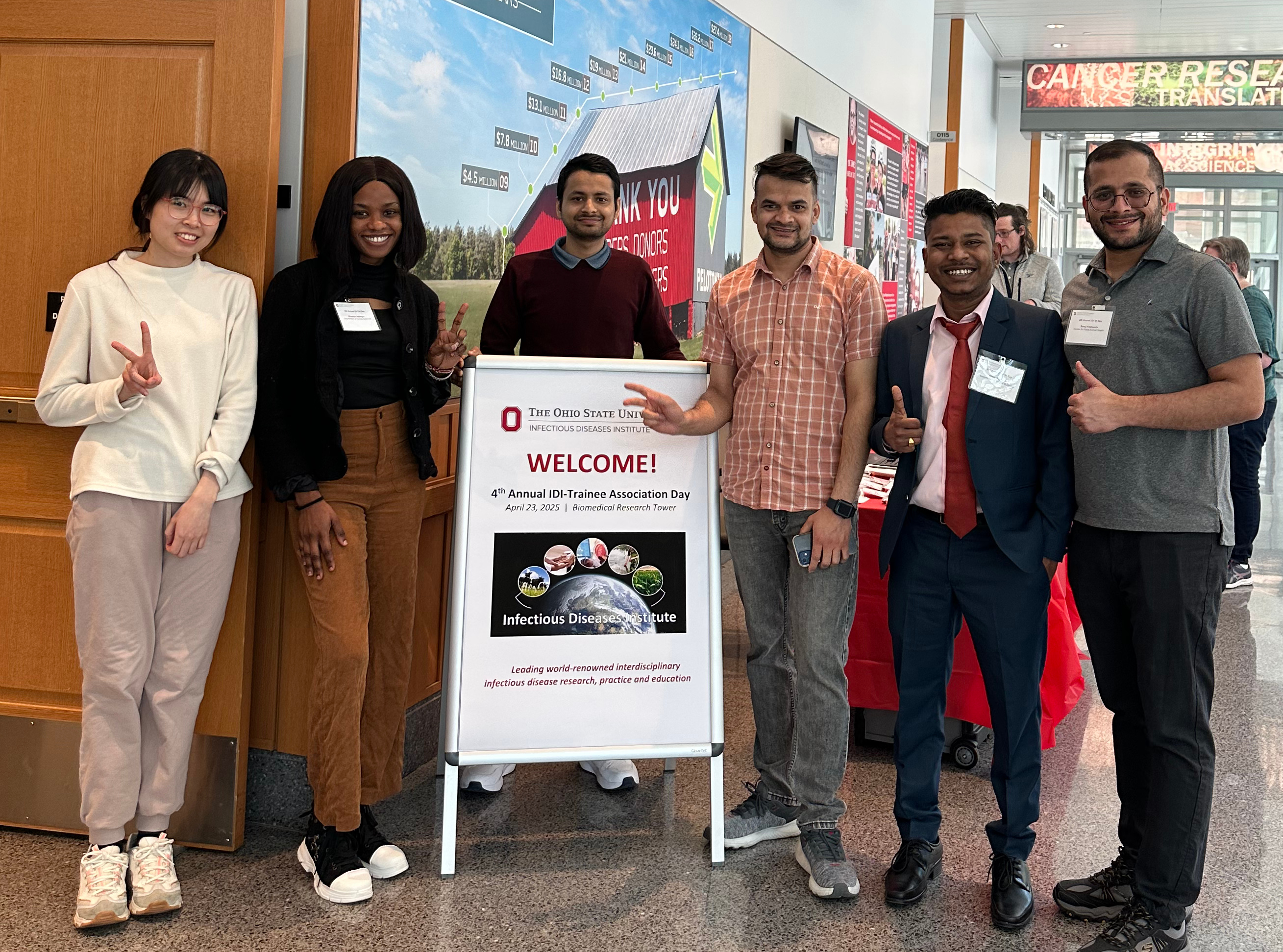 Six individuals stand around a large welcome sign for the 4th Annual IDI Trainee Association Day at The Ohio State University’s Infectious Diseases Institute, held on April 24, 2023, at the Biomedical Research Tower.